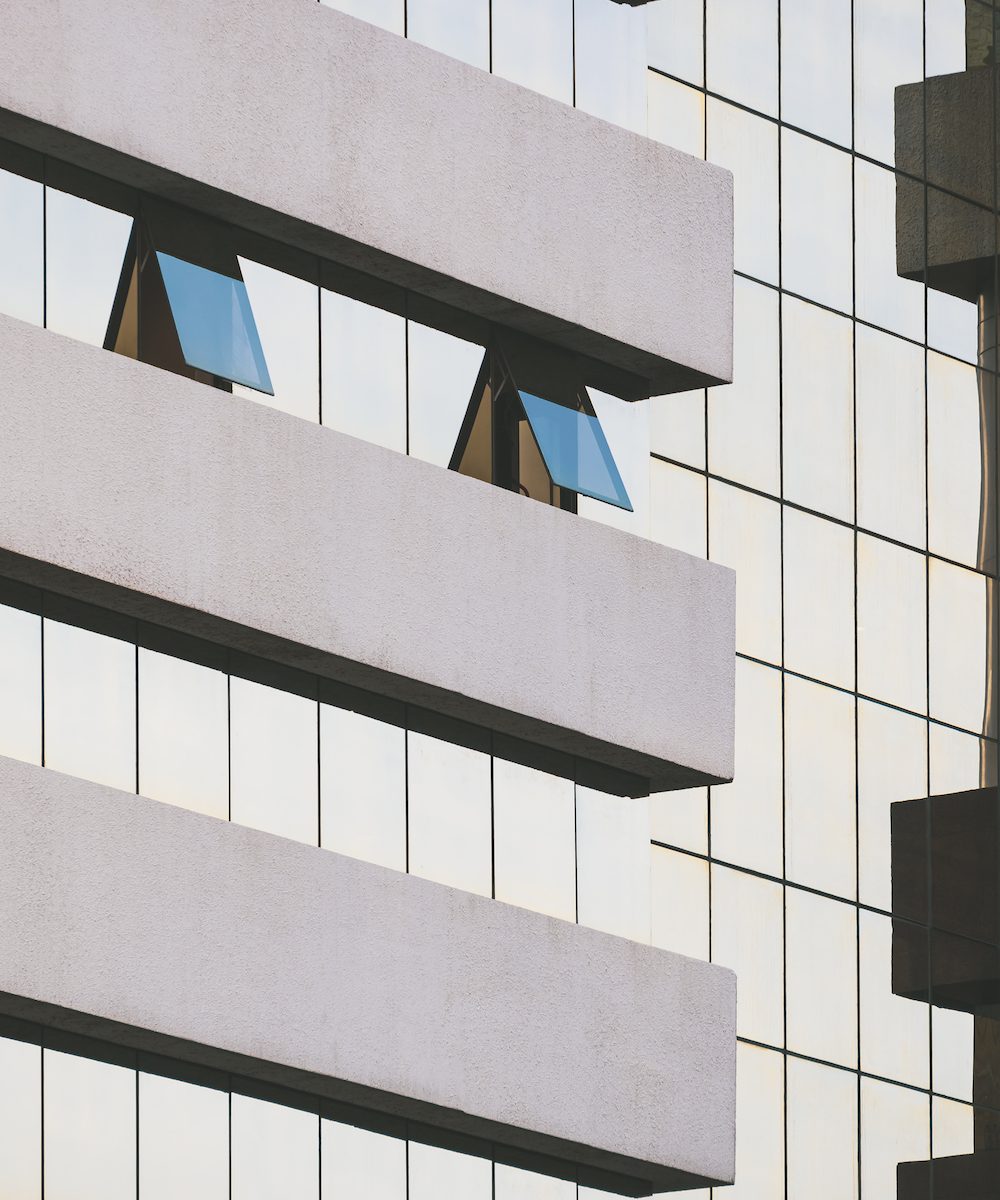 Focus on 2 blue glass windows that are opening on modern high glass office building wall in vertical frame