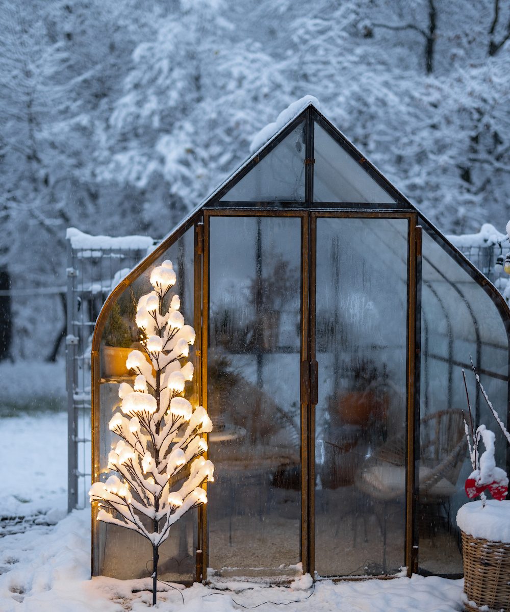 Beautiful snowy yard with vintage greenhouse and glowing tree garland. Concept of New Year holidays and winter magic